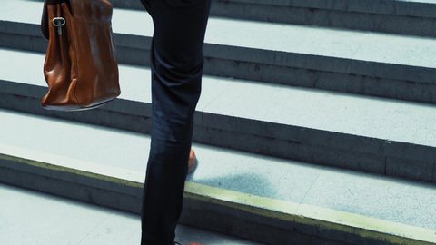 Close up on young man feet in a business suit runs upstairs out of the underground with a suitcase in his hand. Slow motion. Business on the go. Business concept. Prores 422.
