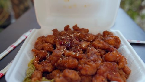 This closeup video shows an order of delicious chinese takeout sweet and sour orange chicken being opened in a reveal by an anonymous hand.