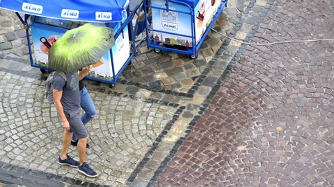 Lviv, Ukraine - July 31, 2018: Aerial high angle above view of old town market square, cobblestone street, people, two young women walking under umbrella closeup panning during rain, wet floor