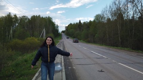 Girl walks along empty road and tries to catch car hitchhiking