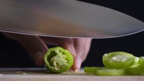 Chef's hand slices fresh green chilli on a wooden chopping board on the kitchen table to cook for customers.