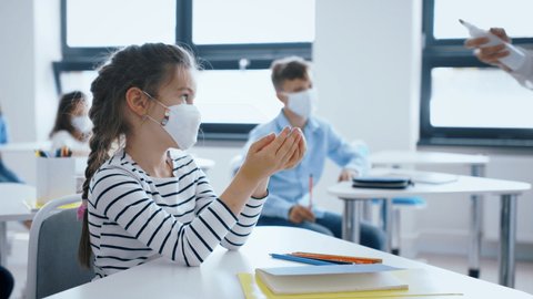 Teacher, children with face mask at school after lockdown, disinfecting hands.