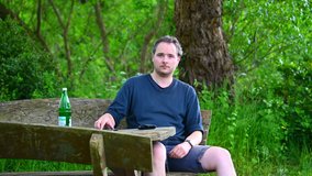 a man sits on a wooden bench in nature, enjoys the summer day and uses his cell phone to take a selfie
 - Powered by Shutterstock - Get 15% off with code: PIKWIZARD15