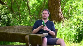 a man is sitting on a wooden bench in nature enjoying the summer day and drinking water from a green glass bottle
 - Powered by Shutterstock - Get 15% off with code: PIKWIZARD15