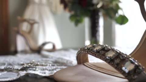 Pair of the high hilled shiny glamour sandals. Luxurious footwear with the wedding dress in the background. Racking focus