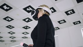 Adult woman is dancing in virtual reality headset and using controllers in an empty playroom full of white neon light. Tracking arc shot, 360 degree, timelapse