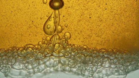 Fuel, yellow, golden oil, poured into a glass vessel in a laboratory, releases bubbles similar to foam.