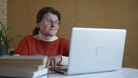 modern old age, elderly pretty woman undergoes online training use video calling on laptop while sitting in kitchen at table