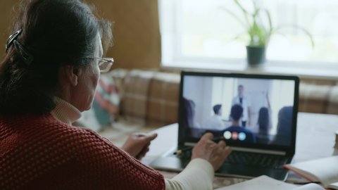 remote training, modern elderly woman undergoes distance learning during an online conference using video call on laptop sitting at table outside window