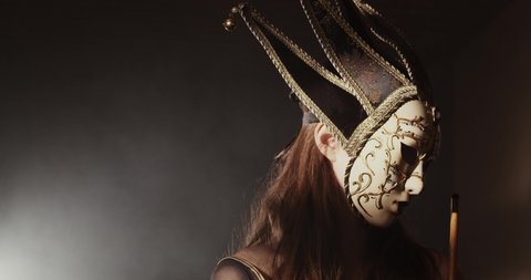 Mysterious, masked person in a dark, foggy room. Haze behind a fantasy figure. Sexy woman wearing venetian mask, looking at the camera.
