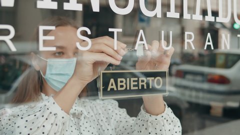 cafe or restaurants and business reopen after coronavirus quarantine is over. woman with face mask turning a sign from closed to open on a door shop. small business after post covid lockdown. Spain