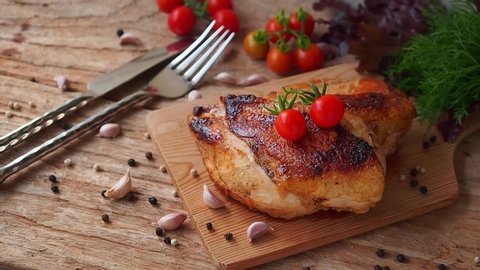 Chicken steak with herbs and fresh cherry tomato on top serve on wooden cutting board.