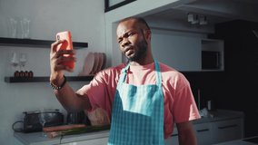 Black young appealing man in apron talking on smartphone online video call conversation in the kitchen. Cooking chef. Technology and people. Communication concept.