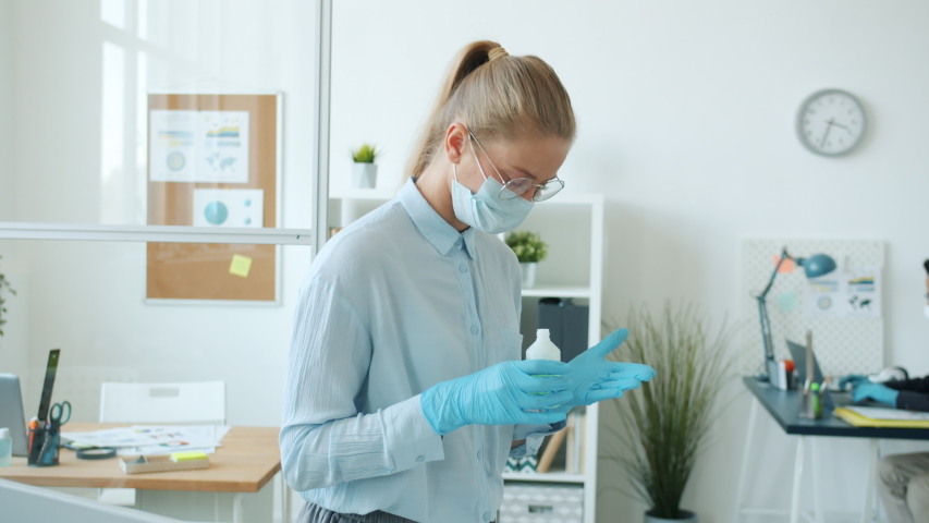 Office employees Middle Eastern man and Caucasian woman are using hand sanitizer and talking during corona virus pandemic working offline wearing face masks. | Shutterstock HD Video #1053639800