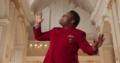 Cheerful african american gospel music singer performing in house of prayer. Young man in red suit singing emotionally and moving in rhythm to music. Concept of people and religion.