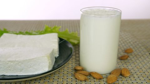 Pan shot of beautifully placed dairy products on a table on white background. Closeup shot of a glass of milk, fresh paneer, processed cheese, butter, and curd placed on the kitchen mat