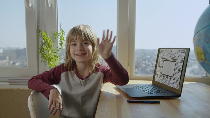 Child studing online by conference call using laptop. Boy smiling, waving hand, looking to camera.Screen with optional corner pin markers for screen replacement. Education at home concept. 60fps