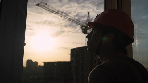 Silhouette Portrait Dirty Building Worker on Background Construction Crane and Beautiful Sunset. Handsome Caucasian Serious Man in Hard Hat Filthy Job and Physical labor. People Working Equipment.