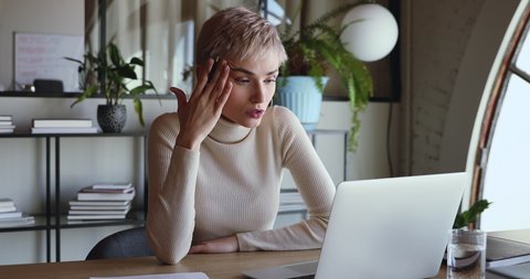 Concerned stressed young business woman feeling tired thinking of difficult online problem solution looking at laptop at workplace. Serious female employee frustrated about overwork in office concept.
