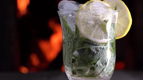 Lemonade with mineral water, lemon ,mint and ice closeup rotates on a wooden table before cozy fireplace. Non alcoholic drink.