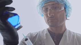 The face of a medic who fills a syringe from a bottle with blue liquid The face of a man in a protective mask and hands in rubber gloves - Powered by Shutterstock - Get 15% off with code: PIKWIZARD15