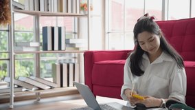 Young Asian business woman freelance work from home using laptop and smartphone to communicate with customer in living room