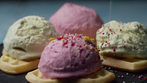 Homemade waffles with color ice ream topping rotating. Pastry topping falling on pink and green ice ream balls on waffles in slow motion.