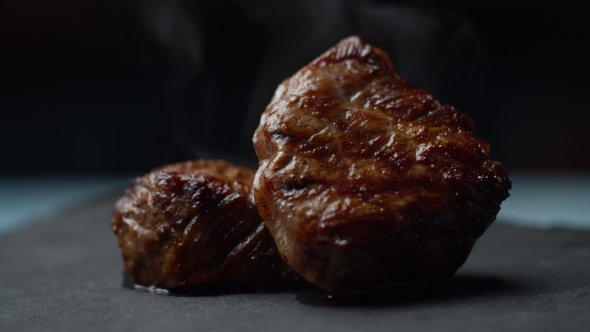 Close up of beef steak rotating on black background in slow motion. Two pieces of filet mignon with smoke. Royalty-Free Stock Footage #1053661919