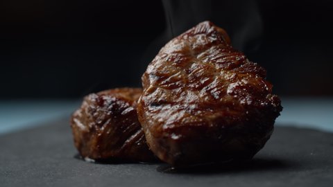Close up of beef steak rotating on black background in slow motion. Two pieces of filet mignon with smoke.