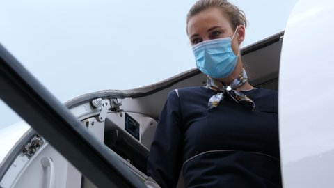 Flight Attendant with Mouth Mask Opening Aircraft Door. Low Angle.