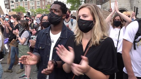 AMSTERDAM, NETHERLANDS – 1 JUNE 2020: Mixed race couple in Amsterdam protests against police violence and racism in support of demonstrations in the US. Covid-19 coronavirus pandemic face masks.