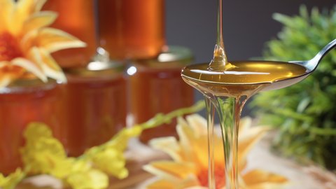 Sweet golden honey dripping, healthy liquid nectar flowing onto metal spoon and dropping down. Jars with natural bee product prepared for traditional beekeeping fair