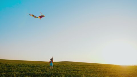 Carefree little girl runs with kite through meadow. Happy kid launch kite in air at golden sunset, playing in field, beautiful landscape, slow motion. Concept of freedom, childhood, summer activity