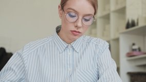 A focused calm young woman architect wearing glasses is working with paper documents at workplace