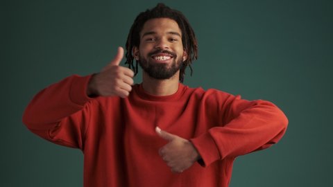 A cheerful funny young african american man is doing a thumb-up gesture isolated over green wall background in studio