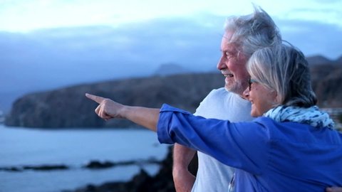 two happy and active seniors or mature people having fun together at the beach looking at the sea or ocean - pensioners enjoying their vacations traveling 