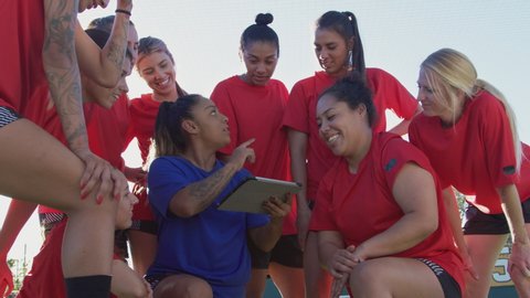 Female coach discussing tactics with womens soccer team using digital tablet before match - shot in slow motion