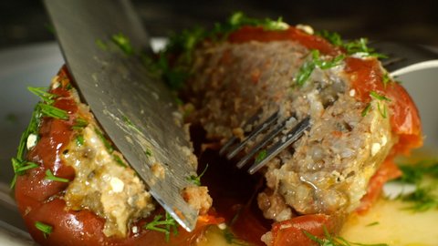 Appetizing stewed bell peppers stuffed with minced rice and pork or beef meat and sprinkled with dill in savoury sauce, are cut into pieces with a knife. Close up.