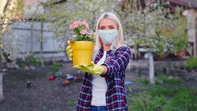 Very charismatic lady with a protective mask in front of the camera in pandemic wearing protective mask holding a flower pot she smelling the flowers and feeling great Coronavirus 2019