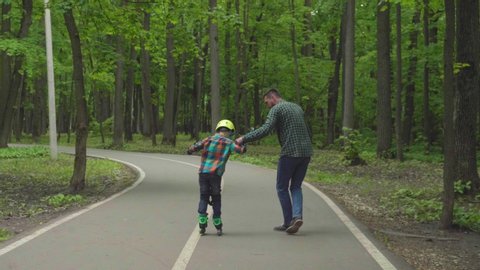 Father and son are preparing for roller skating in the fresh air. father's day. The son learns to roller skating, falls and gets up.