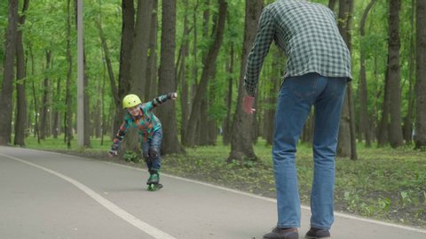 Father and son are preparing for roller skating in the fresh air. father's day. The son learns to roller skating, falls and gets up. Video de stock