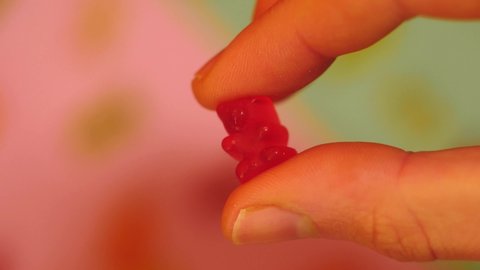 Hand hold and press gummy bear. Jelly candies on colorful background. Candy industry  