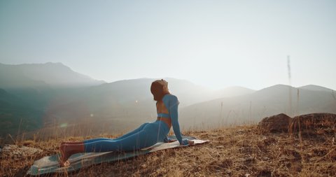 Yoga meditation in mountains. Fit girl doing yoga poses, having training session on cliff during sunrise - healthy way of life concept 4k footage