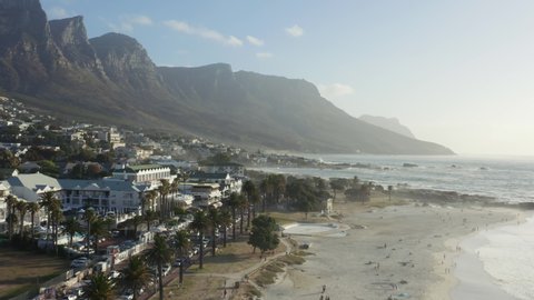 Wide aerial sweeping shot of Camps Bay blue flag beach, with views to the twelve apostles mountains, Cape Town, South Africa