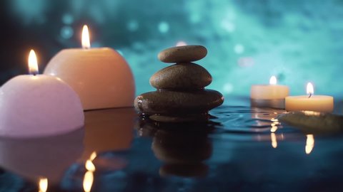 burning candles in water, reflection of stones on abstract blue background, water drops falling. slow motion. Close up. Concept: relaxation, wellness, body care, spa, nature, aromatherapy and scents
