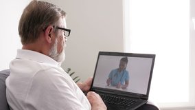 Telemedicine. Elderly man sitting with a laptop on the couch in her apartment consults her doctor via the Internet.