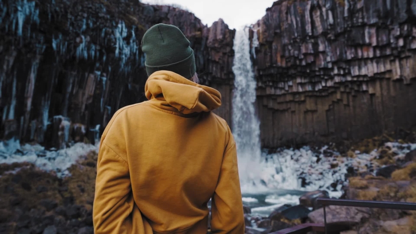 A young woman standing and looking at the bottom of a waterfall in Iceland.