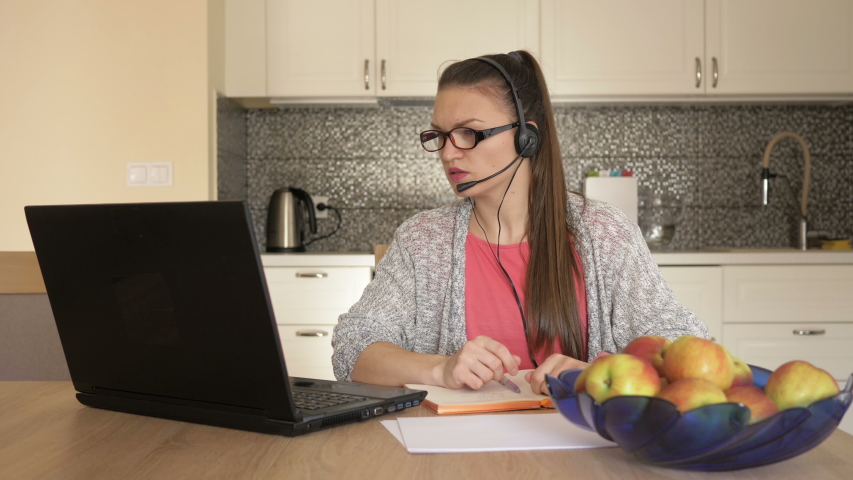 Young woman with headset in front of laptop at the table, online customer consultation.