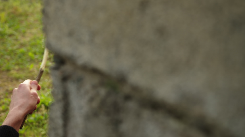 Young man peeling stick with knife