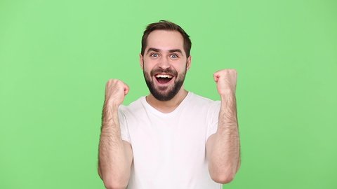 Bearded fun young guy 20s in white t-shirt isolated on green chroma key background studio. People sincere emotions lifestyle concept. Looking camera shocked surprised say wow yes doing winner gesture
